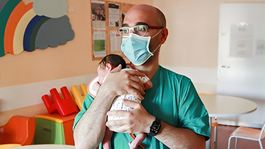 Nurse wearing a mask while holding an infant safely.