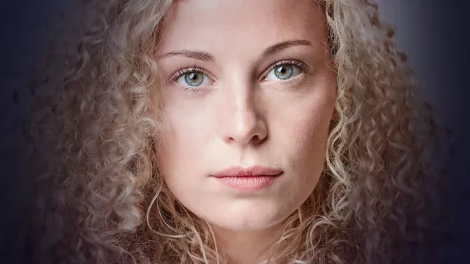 A young woman with curly hair faced directly at camera