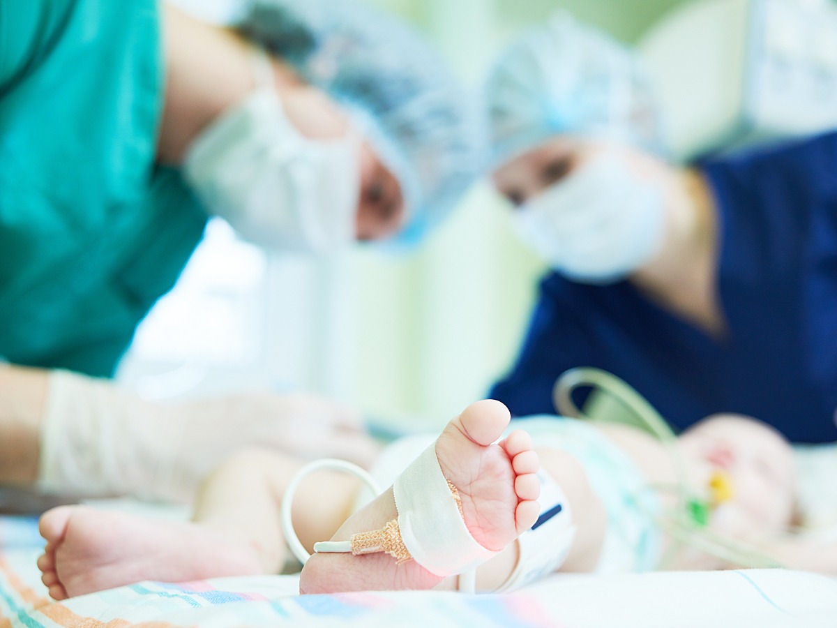 Close-up of an infant's feet, with two doctors attending to the infant in the background.
