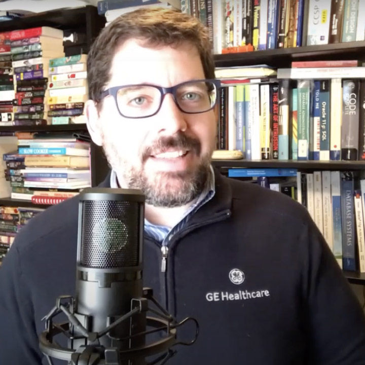 Brian green with a podcast microphone in front of bookshelf