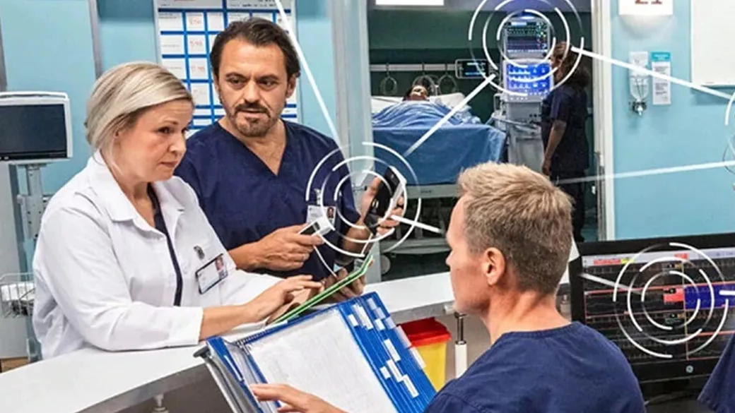 Two clinicians standing around a desk. A third clinician is seated at the desk talking to the other clinicians.