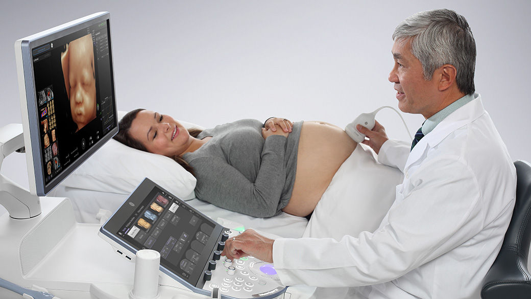 A clinician using a Voluson™ Ultrasound Systems for Labor and Delivery on a pregnant woman laying in a hospital bed.