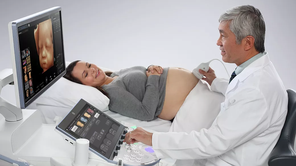 A clinician using a Voluson™ Ultrasound Systems for Labor and Delivery on a pregnant woman laying in a hospital bed.