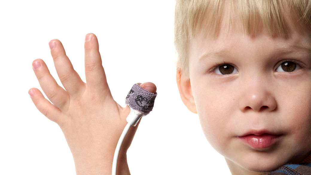 Child looking at the camera and holding his hand up. His thumb has a monitor on it.