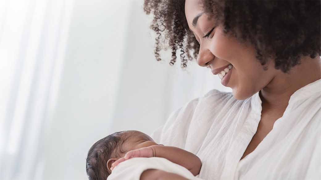 A woman smiling while holding a newborn baby.