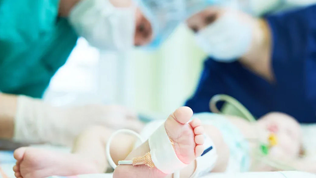 Clinicians attending to an infant who has a monitoring device attached to their foot.