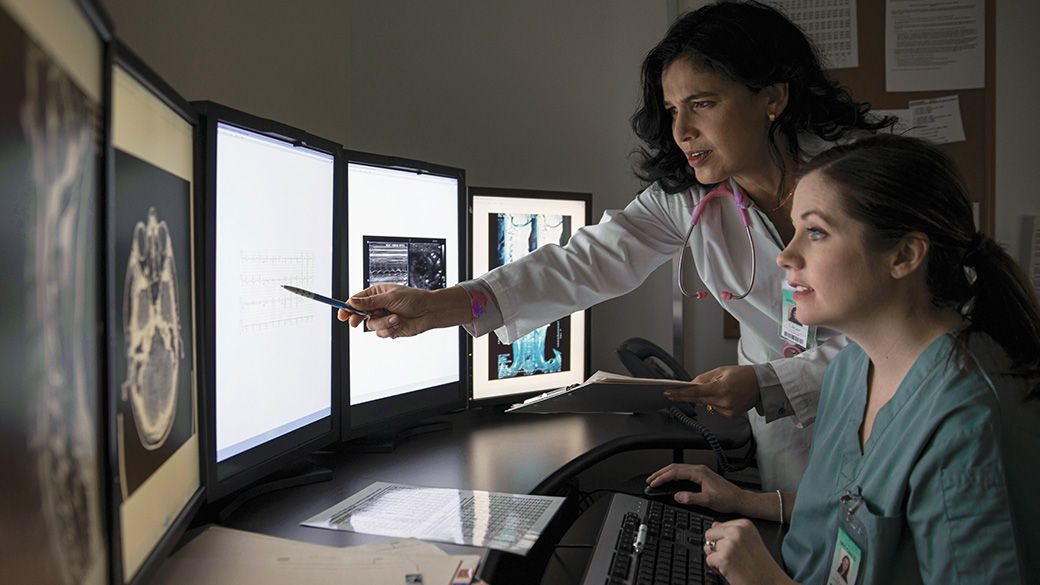 Two healthcare providers looking at five computer monitors