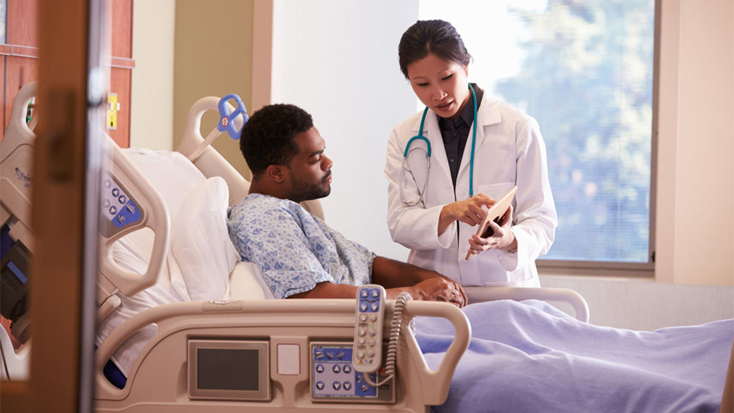 Patient laying in hospital bed with a doctor standing and pointing at a tablet