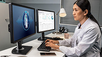A clinician working at two computer monitors