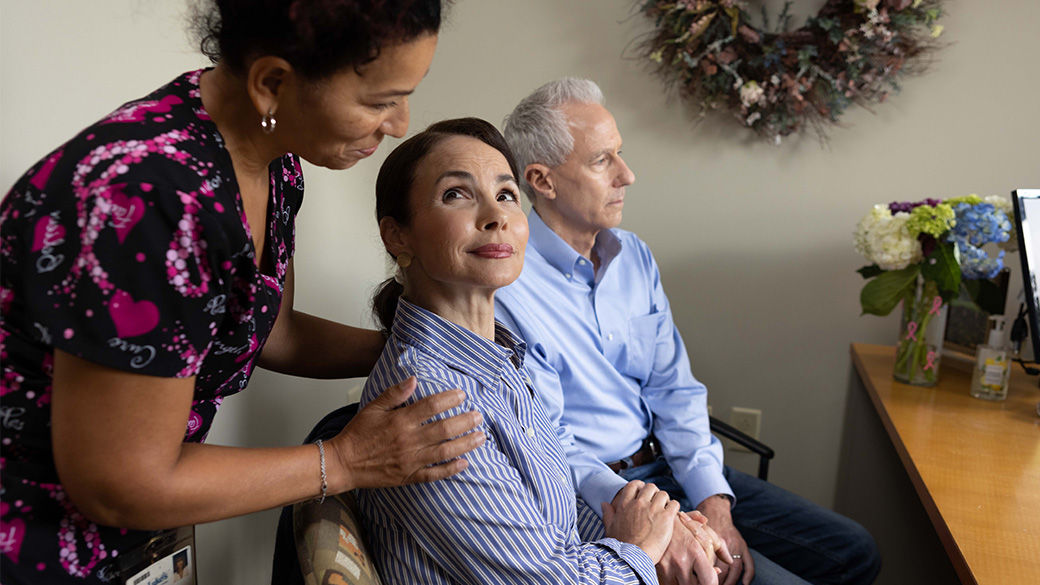 Image of a woman with her hand on the shoulder of another woman seated beside a man.