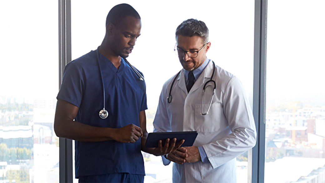 Image of two clinicians having a discussion, with one holding a tablet in their hand.
