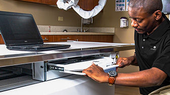 Image of a man repairing a piece of computer equipment in an exam room.