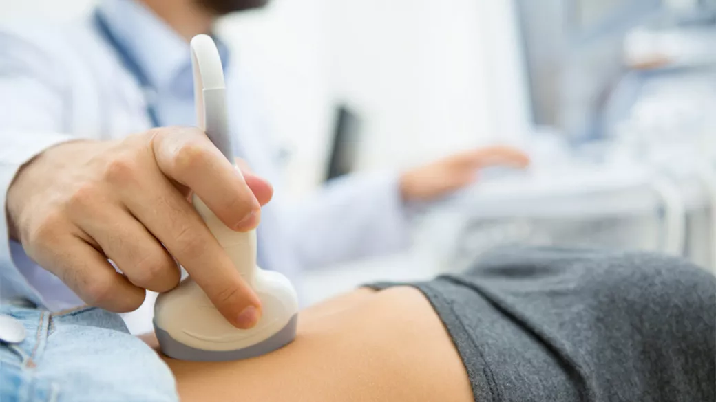 Close up of clinician's hand holding an ultrasound probe on a patient's abdomen