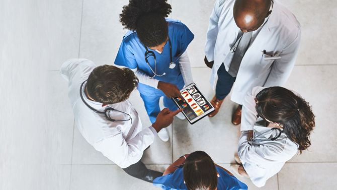 looking down at group of five healthcare practioners gathered around tablet
