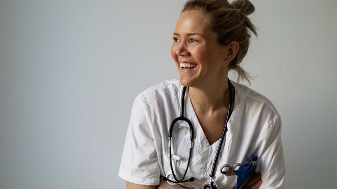 smiling blond female nurse in white scrubs looking to left