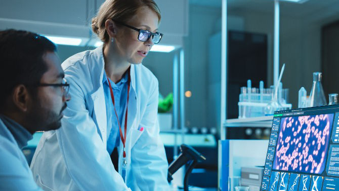 two clinicians in lab coats look at data visualization on laptop screen