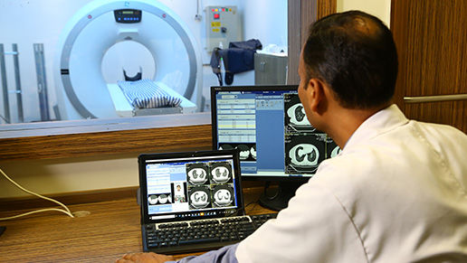 Physician looking at MRI images on a laptop with a MRI machine in the background