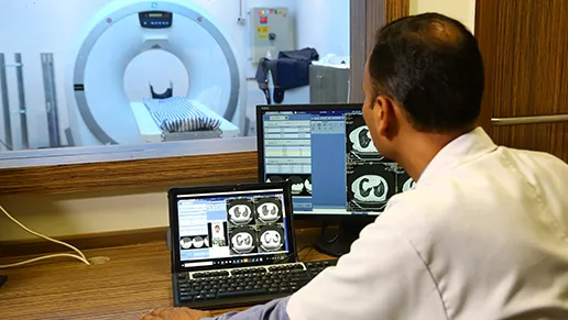 Physician looking at MRI images on a laptop with a MRI machine in the background