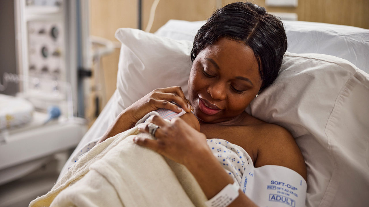 A mother holding an infant in a hospital bed.