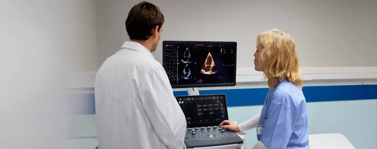 Ultrasound imaging system with two healthcare professionals reviewing cardiac scan images on a monitor.
