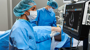 Doctor operating on a patient while another doctor is looking at the Venue monitor