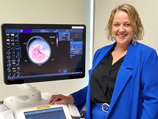 Woman standing and smiling next to a sonograph on a monitor next to her. 