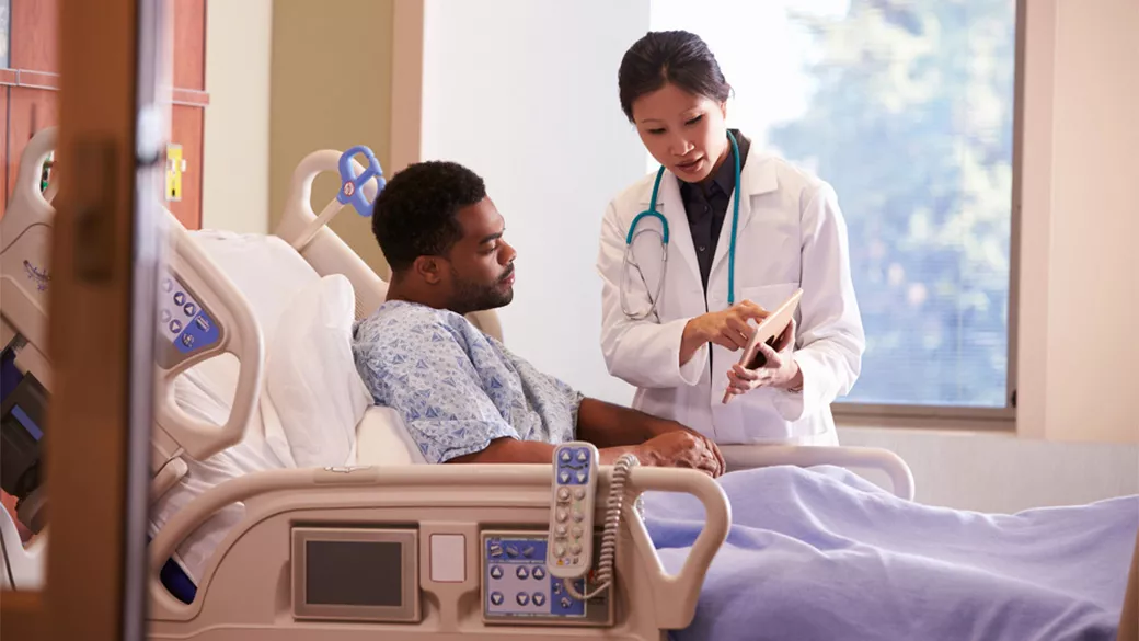 Patient laying in hospital bed with a doctor standing and pointing at a tablet