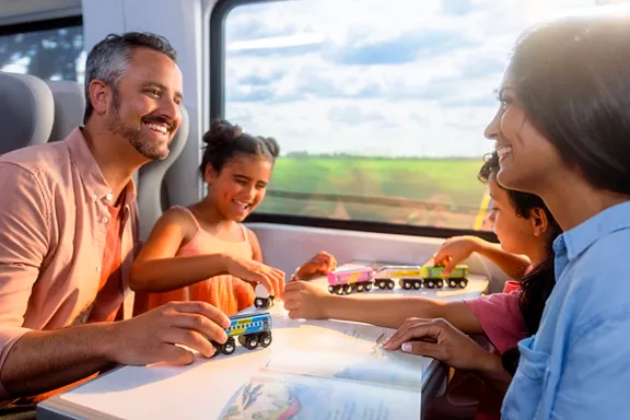 A family of four seated at a table aboard a Brightline train with the young kids playing with a toy train
