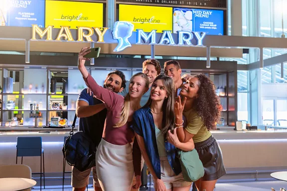 A group of people taking a selfie in front of Brightline Orlando Station's Mary Mary bar