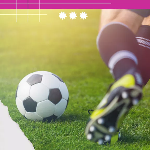 A soccer player is captured mid-action, kicking a black and white soccer ball on a vibrant green grass field. The athlete is wearing black socks and cleats, with only the lower legs visible. The scene is brightly lit, suggesting an outdoor setting with energetic movement. Graphic elements and three white stars are visible in the upper portion of the image.