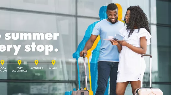 A man and woman smiling while standing outside a resort with their luggage.