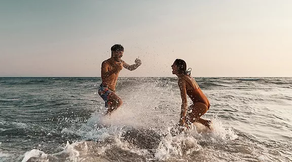 Young playful couple having fun while splashing in summer day at sea. Copy space.