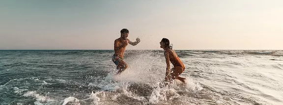 Young playful couple having fun while splashing in summer day at sea. 