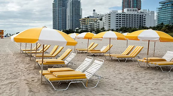 Outdoors chairs and yellow umbrellas on empty beach. Skyscrapers are visible in the background.