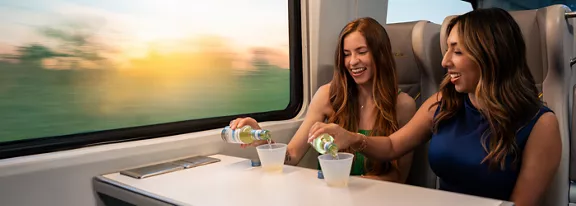 Two ladies sitting on a table with two drinks riding the Brightline train.