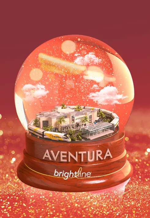 An Aventura snow globe featuring a Brightline train on a glittery red holiday background.