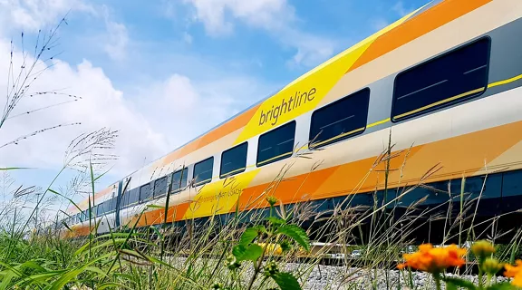 Side view of Brightline's Bright Orange train passing on a railroad