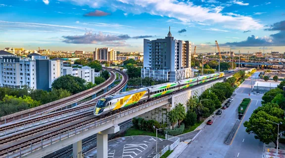 A Brightline train moving through Miami with a Brightline yellow logo overlay