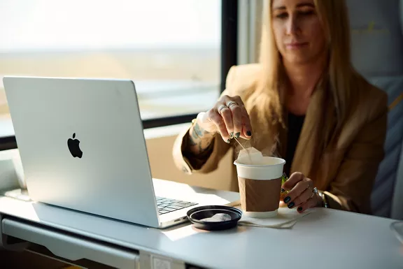 A woman working on her laptop and enjoying a hot tea while riding a Brightline train.