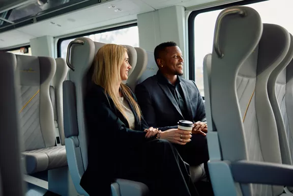 A man and businesswoman smiling and looking out the window of a Brightline train.