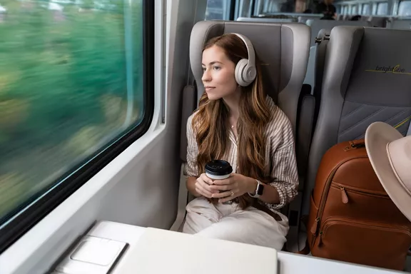 A woman listening to music and drinking coffee while riding on a Brightline train.