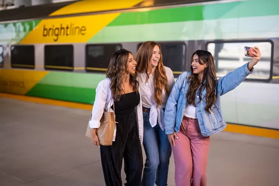 Three women posing for a selfie with a Brightline train car in the background.