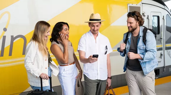 Four friends standing with their luggage beside a Brightline train car.