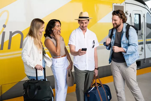 Four friends standing with their luggage beside a Brightline train car.