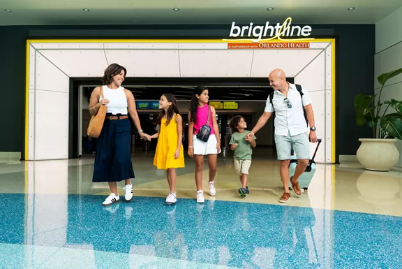 A man and woman walking with their three young children through the Brightline station lobby.