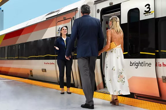 A Brightline employee greeting a couple walking on the train platform, getting ready to board a Brightline train