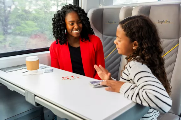 A woman and her young daughter playing cards while riding on a Brightline train.