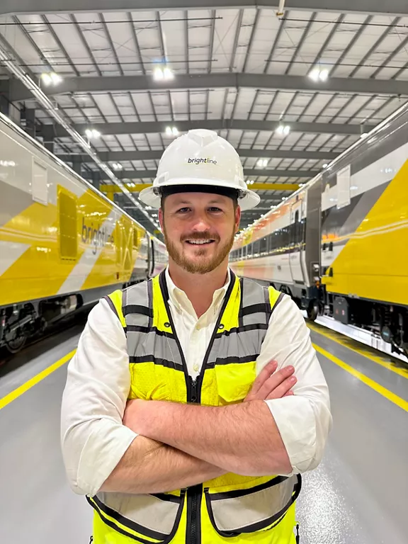A Brightline teammate in a white construction hard hat and safety vest