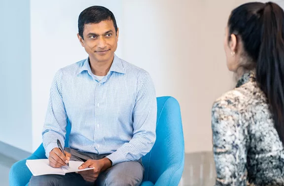 An employee taking notes while in conversation with another coworker not facing the camera