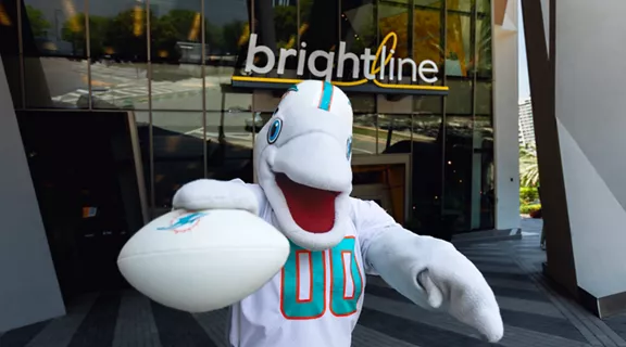 Miami Dolphins mascot T.D. posing with a white Miami Dolphins football outside of Brightline MiamiCentral station